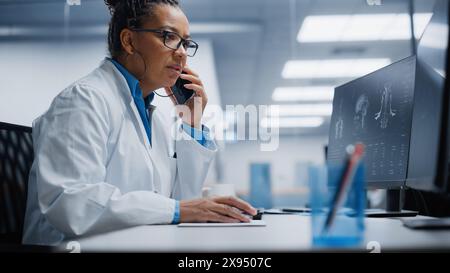 Medical Hospital Research Lab: Black Female Neurosurgeon Using Computer with Brain Scan MRI Images, Talking on the Phone with Sick Patient. Health Care Neurologist Finding Treatment. Energetic Arc Stock Photo