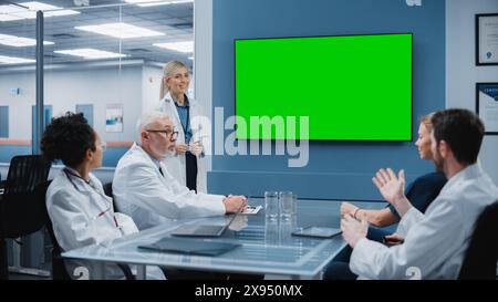 Hospital Conference Meeting Room: Female Doctor Presents Chroma Key Green Screen TV to a Team of Medical Professional. Research Scientists Discuss Patient Treatment, Drugs and Medicine Development Stock Photo