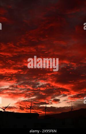Stunning sunset with vibrant red and orange clouds over wind turbines, creating a dramatic and picturesque skyline Stock Photo