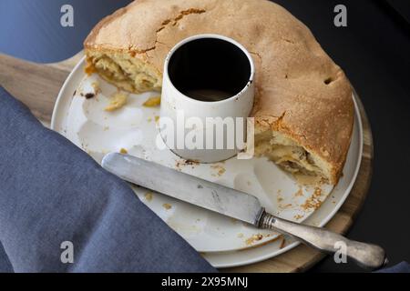 Top view of an apple sponge cake in a white detachable tin with vintage knife on a black background with dark blue drapery in natural light Stock Photo
