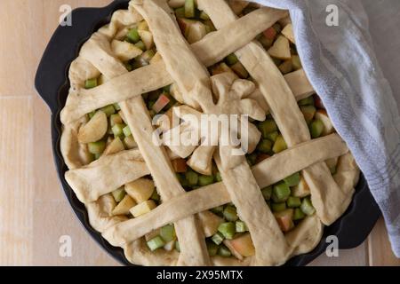 Table top food photography of ready to bake open yeast dough Rhubarb and Apple Pie in a round black ceramic backing form standing on wooden table Stock Photo