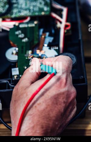 A technician is repairing a circuit board of an electronic device in a workshop during the afternoon. His hands are seen using tools to fix components Stock Photo