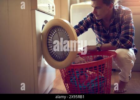 House, washing machine and man with laundry in kitchen, spring cleaning and loading in washer and clothes. Home, guy and person in apartment Stock Photo