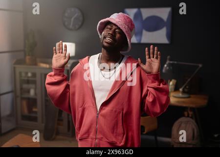 Waist up portrait of Black young man wearing pink hip-hop outfit looking at camera while dancing indoors copy space Stock Photo