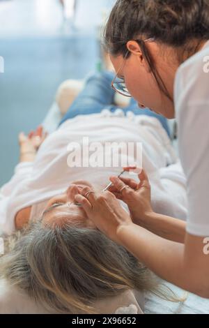 Young girl giving an acupuncture treatment to an elderly lady on the stretcher Stock Photo