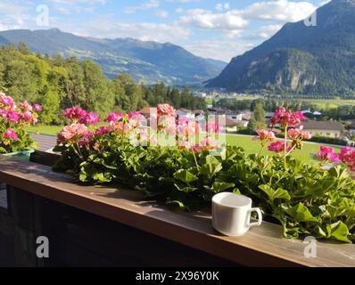 Idyllic view from balcony with geranium flowers and coffee cup in the village of Wiesing towards green valley with Alps and Lake Achensee in Tyrol, Au Stock Photo