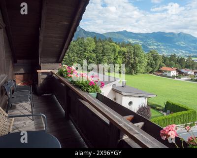 View from wooden balcony with geranium flowers, table and chairs in the village of Wiesing towards green valley with Alps and Lake Achensee in Tyrol Stock Photo