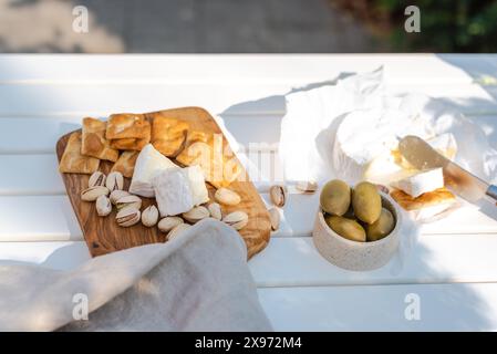 Wine appetizers namely pistachios, camembert cheese, saltine crackers and olives on a white table outdoors. Stock Photo