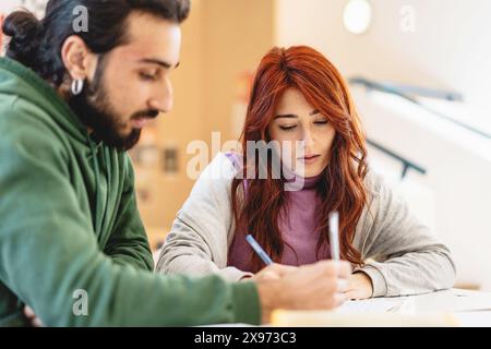 Two focused students writing notes together in a classroom setting, collaborative study, young adults learning, academic teamwork, engaged and concent Stock Photo