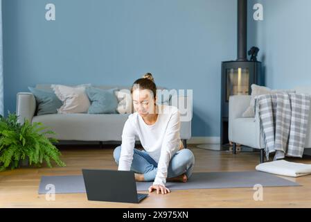 Young woman in sportswear is using her laptop to conduct an online yoga class from home. Women's health. Online communication concept. Stock Photo