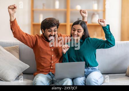 Man and Woman Sitting on Couch With Laptop, Celebrating Success Stock Photo