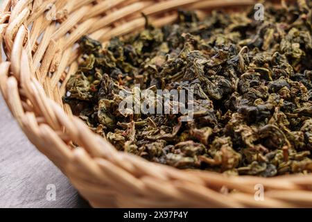 Dry rolled gunpowder green tea leaves in an eco rustic rattan bowl on a board. Healthy herbal drinks. Source of Antioxidants. Stock Photo
