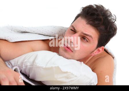 close up of a young discontent man in bed waking up with tired and  annoyed  facial expression Stock Photo
