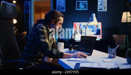 Skilled computer scientist writes code on laptop screen while in living room office using programming languages. Self employed IT specialist working on fixing database errors from home, camera B Stock Photo