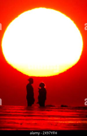 Isle Of Palms, United States. 29th May, 2024. A couple, silhouetted by the sunrise, takes a selfie on the beach as a heat wave sweeps across the region bringing temperatures into the 90's, May 29, 2024 in Isle of Palms, South Carolina. Credit: Richard Ellis/Richard Ellis/Alamy Live News Stock Photo