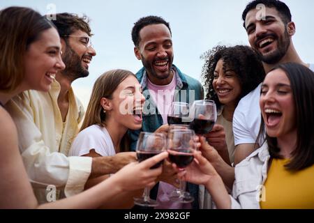 Portrait of multi-ethnic laughing young people toasting glasses red wine outdoor Stock Photo