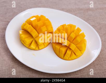 Two halves of ripe yellow mango cut into cubes lie on white round plate Stock Photo