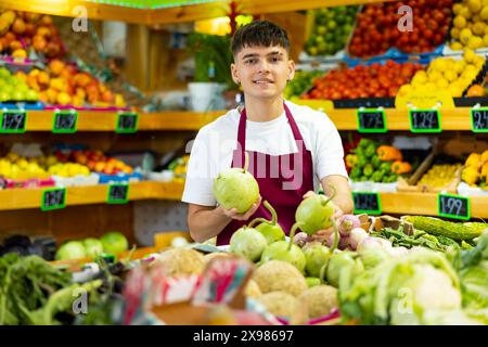 Young salesman working and posing in store near counter with round bottlegourd vegetable Stock Photo