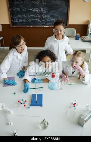 Vertical high angle view shot of kids wearing lab coats and goggles looking at chemical reaction while experimenting in class Stock Photo