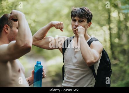 Group of friends hiking in the forest and flexing muscles while taking a snack break Stock Photo