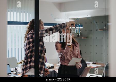 Business professionals actively brainstorming and strategizing with sticky notes on glass wall in a modern office environment Stock Photo