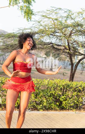 Happy woman dancing in red costume outdoors, curly hair, expressive movement. Stock Photo