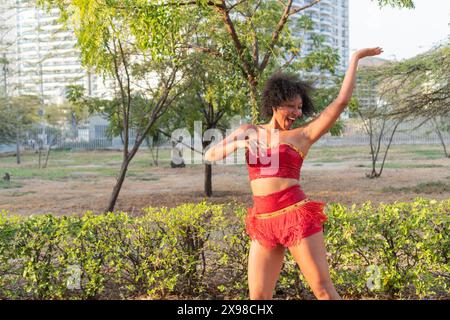 Joyful woman dancing in red costume outdoors, curly hair, expressive movement. Stock Photo