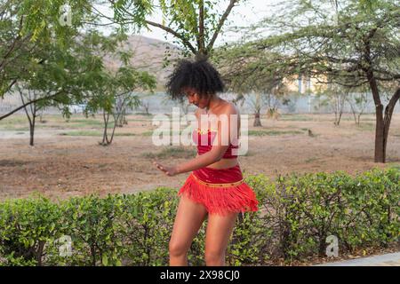 A woman in a red dance outfit performs gracefully in a natural outdoor setting with greenery and distant hills, showcasing movement and artistic expre Stock Photo