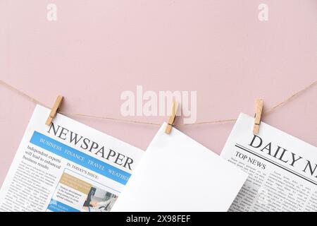 Newspapers and blank sheet of paper hanging on rope against pink background Stock Photo