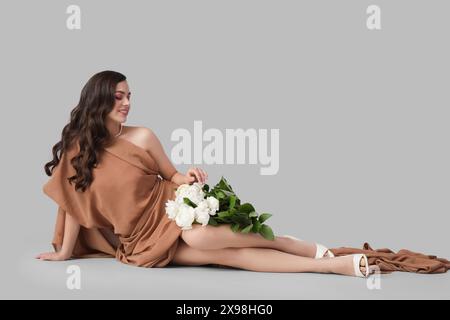 Beautiful young woman with bouquet of white peony flowers sitting on grey background Stock Photo