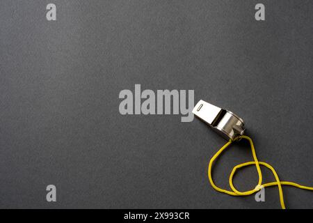 Top view of metal whistle with yellow string on dark gray background Stock Photo