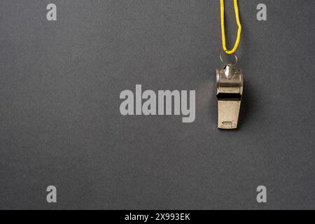 Top view of metal whistle with yellow string on dark gray background Stock Photo