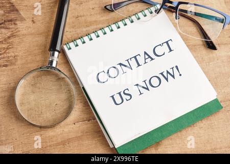 CONTACT US NOW word inscription on a notebook with a magnifying glass and glasses on a vintage background Stock Photo