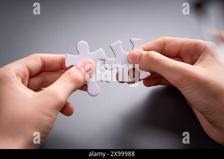 Hands fitting two puzzle pieces together on a gray background, symbolizing teamwork, connection, problem solving, cooperation, and partnership Stock Photo