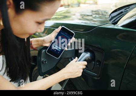 Cropped image of ev owner using smart charger app when charging electric car Stock Photo