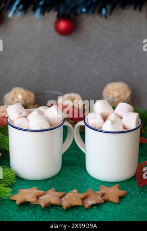 Two mugs with hot chocolate, topped with marshmallow, near several star-shaped gingerbread cookies, surrounded by a festive seasonal background Stock Photo