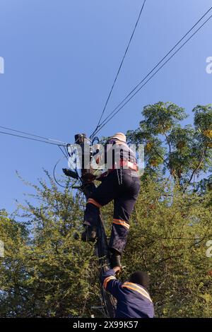young african man technician, upgrading copper cable with fiber optic cable on a wooden pole Stock Photo