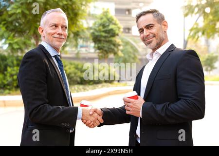 Two successful businessmen standing shaking hands, looking at the camera. Stock Photo
