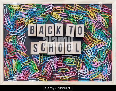Black board with colorful paper clips and wooden cubes with the text: Back to school Stock Photo