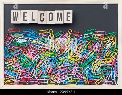 Black board with colorful paper clips and wooden cubes with the text: Welcome Stock Photo