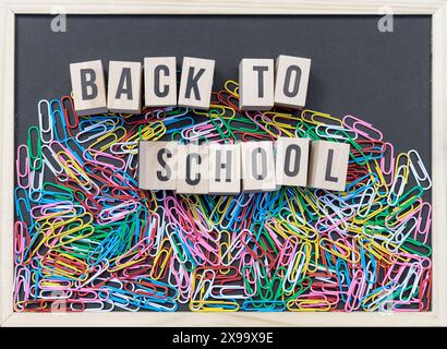 Black board with colorful paper clips and wooden cubes with the text: Back to school Stock Photo