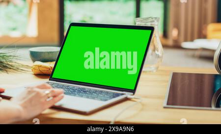 Close Up Green Screen Mock Up on Laptop Computer. Device is Used on a Kitchen Table in a Modern Home. Person Uses Touch Pad for Scrolling the Web. Sunny Modern Home with Healthy Lifestyle Atmosphere. Stock Photo