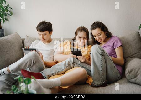 Curious siblings using wireless technologies with down syndrome sister sitting on sofa at home Stock Photo