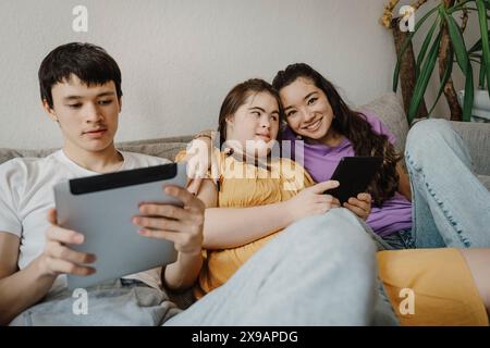 Portrait of smiling woman sitting with down syndrome daughter and brother using digital tablet on sofa at home Stock Photo