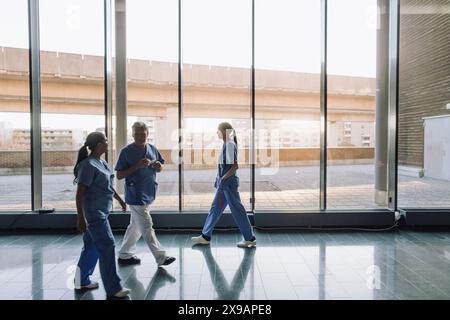 Male and female healthcare workers discussing while walking in corridor of hospital Stock Photo
