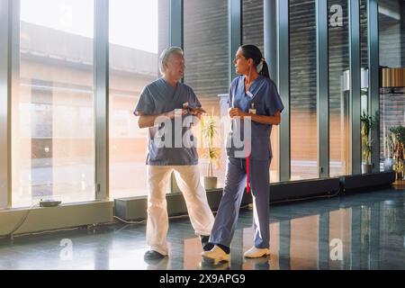 Senior male and female doctors discussing while walking in corridor of hospital Stock Photo