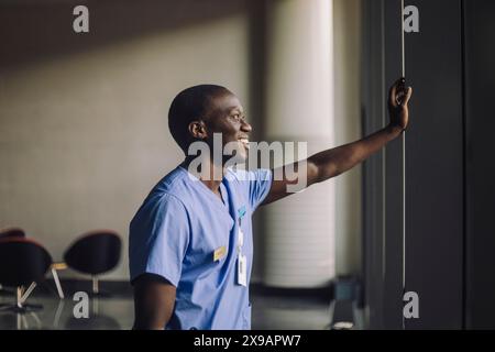 Smiling male doctor with hand on wall standing at hospital Stock Photo