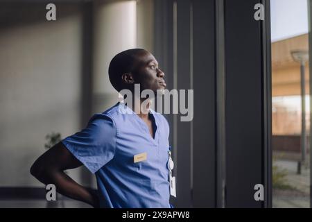 Thoughtful male doctor looking through window while standing at hospital Stock Photo