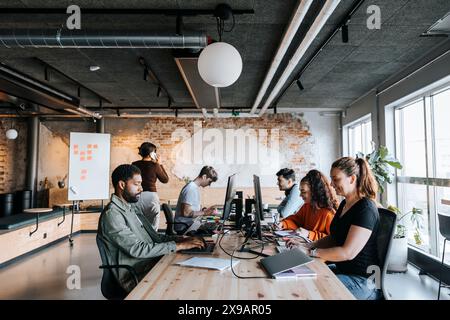 Multiracial male and female entrepreneurs working on computers while sitting at desk in office Stock Photo