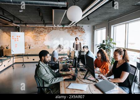 Group of male and female business professionals working on computers at desk in coworking office Stock Photo